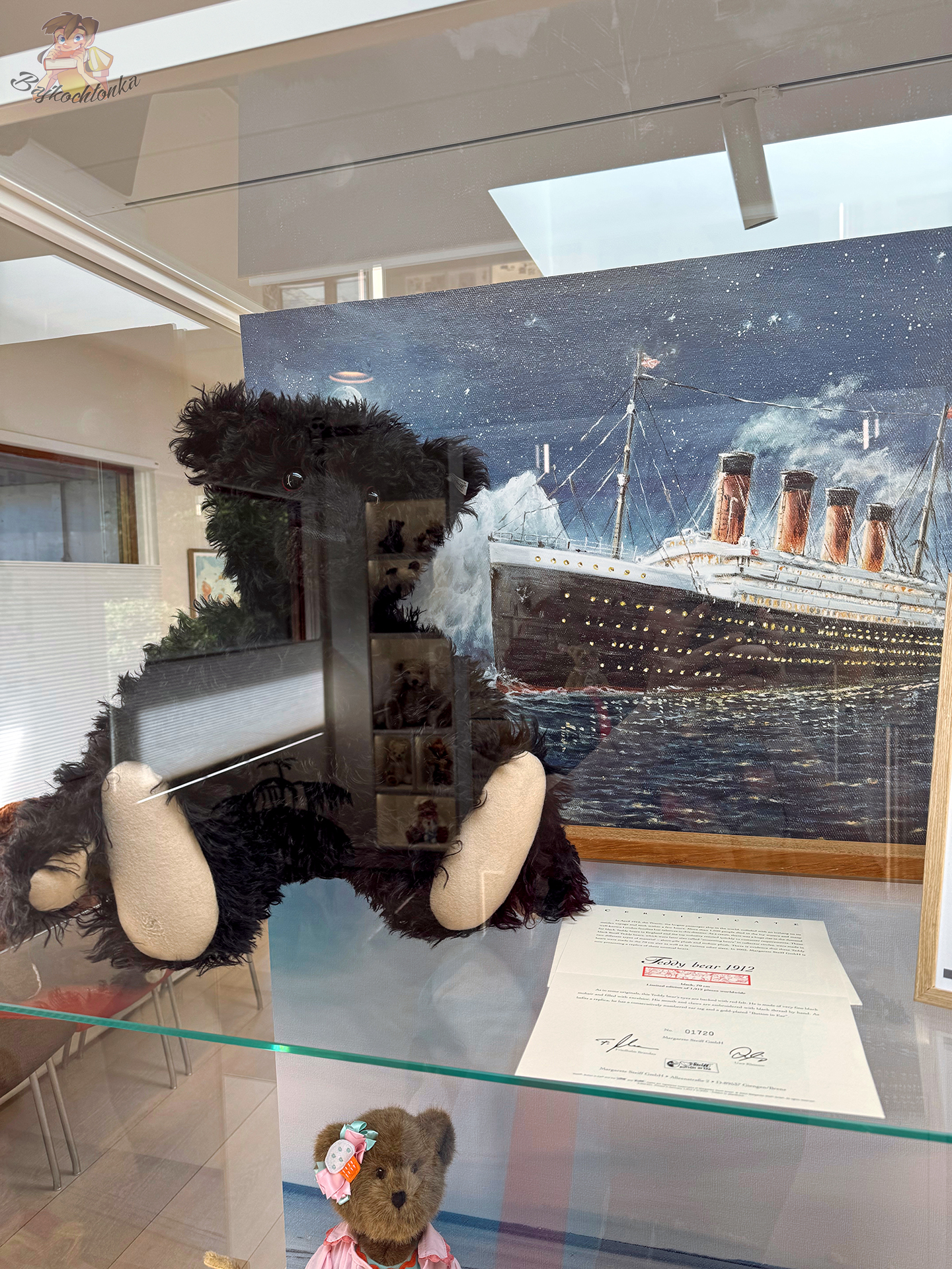 Czarny kolekcjonerski miś na tle obrazu tonącego Titanica, prezentowany w szklanej gablocie Teddy Bear Art Museum w Billund.