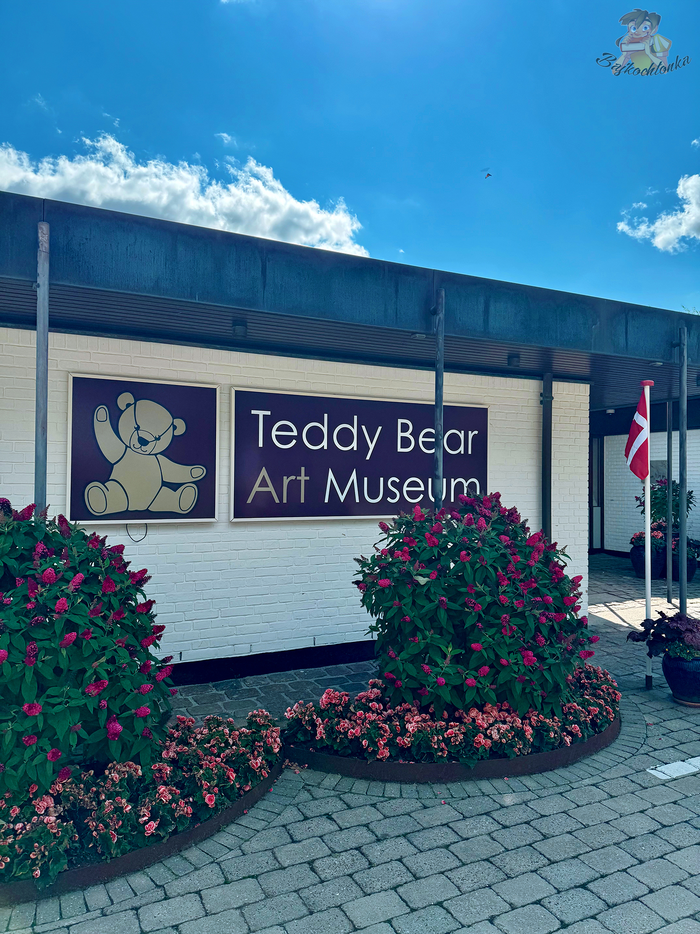 Wejście do Teddy Bear Art Museum w Billund w Danii, z charakterystycznym szyldem przedstawiającym pluszowego misia.